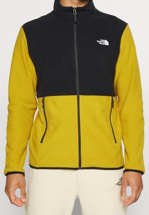 Mann trägt eine gelb-schwarze Fleecejacke mit Frontreißverschluss und Reißverschlusstaschen, The North Face-Logo auf Brust und Hose.
