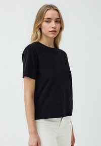 Zwarte t-shirt met korte mouwen, gemaakt van zachte katoen, met een relaxte pasvorm en minimale details, gecombineerd met lichtgekleurde broeken.