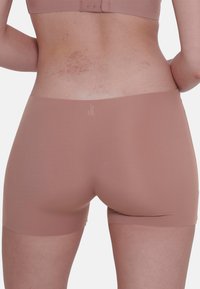 Bodysuit i nude-stof, med en glat tekstur og sømløs design. Båndet er minimalistisk med en diskret logo.