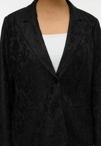 Zwarte kanten blazer met een opstaande kraag, twee knopen en twee voorzakken. De stof heeft een textuur met bloemmotief.