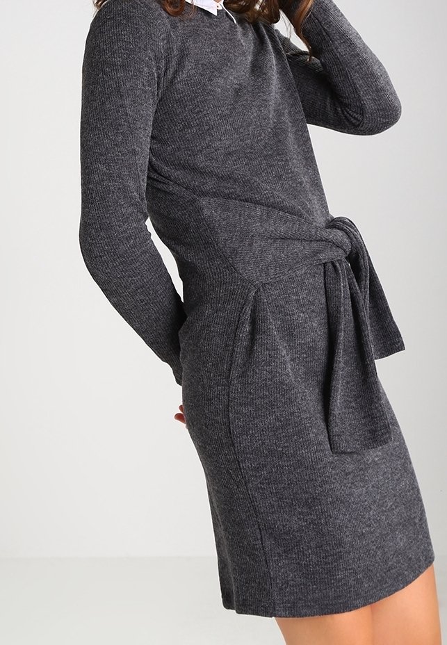 Abito grigio a maglia con maniche lunghe, una cintura annodata in vita, tasche laterali e una texture a costine. Presenta un colletto bianco sottostante.