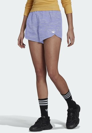 Shorts sportivi di colore viola chiaro con un motivo a onde bianche e un logo ricamato. Abbinati a sneaker nere e calzini neri a righe.