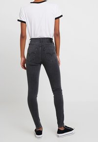 Jeans skinny grises de cintura alta, con un diseño clásico de cinco bolsillos y costuras sutiles, combinados con una camiseta blanca y zapatillas negras.