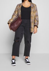 Rutig kavaj i beige och svart, svart spetslinne, trasiga svarta jeans och svarta sneakers. Håller en vinröd läderväska.