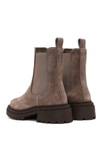 Des bottes Chelsea en daim marron présentent des panneaux latéraux élastiques, une languette et une semelle en caoutchouc robuste avec un profond profil pour une bonne adhérence.