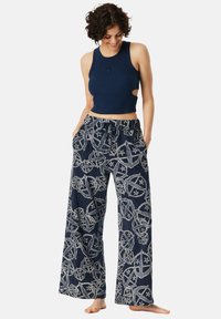 Marineblauwe geknipte tanktop met zijknipsels, gecombineerd met losse, gepatineerde wijde broek met witte patronen en een elastische trekkoord taille.