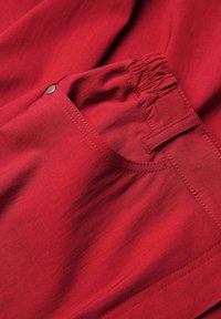 Rode stof met een gladde textuur, voorzien van een elastische tailleband, zijzak met drukknopsluiting en stikdetails.