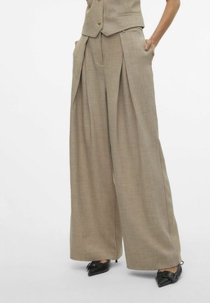 Pantaloni beige a gamba larga con pieghe, realizzati in tessuto testurizzato. Presentano tasche laterali e una vestibilità su misura. Abbinati a scarpe nere con punta.