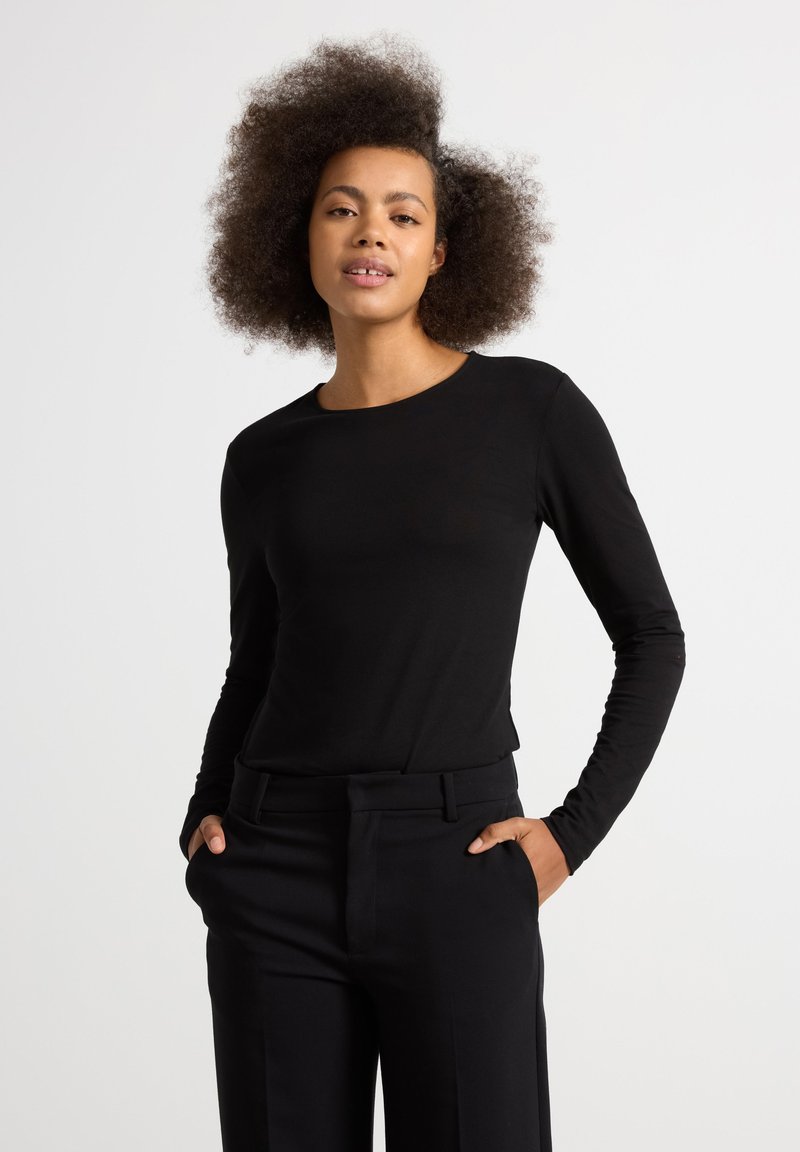 Sort langærmet top med rund halsudskæring, slim fit og glat overflade, parret med højtaljede sorte bukser.