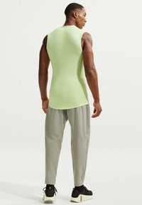 Ανοιχτό πράσινο αμάνικο τοπ, με λεία υφή, συνδυασμένο με ανοιχτό γκρι μπατζάκια που στενεύουν προς τα κάτω με σχέδιο πάνελ, φορεμένα με μαύρα παπούτσια.