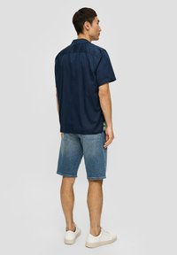 Marineblauw shirt met korte mouwen en een casual snit, gecombineerd met blauwe denim shorts en witte sneakers. Eenvoudig ontwerp, comfortabele pasvorm, zichtbare stiksels.