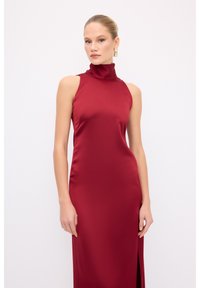 Bordeaux satin kjole med høj hals, ærmeløst design og en sideslids. Den glatte tekstur og den tætsiddende silhuet forstærker det elegante udseende.