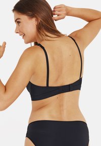 Haut de bikini noir avec des bretelles réglables et un système de fermeture à crochets à l'arrière. Tissu lisse sans motifs, associé à un bas de bikini assorti.