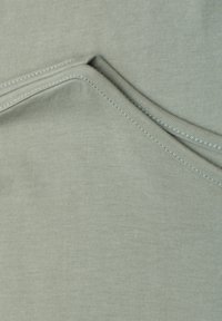 Gros plan d’un tissu vert clair superposé avec des coutures visibles et une texture lisse.