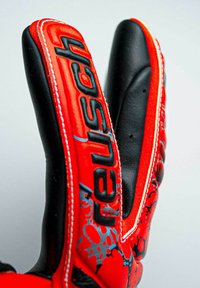 Gants de gardien de but rouges et noirs avec grip en caoutchouc, surface texturée et logo brodé. Les coutures notables en blanc contrastent avec les couleurs.