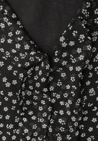 Zwarte stof met een gestructureerd oppervlak, voorzien van een klein wit bloemmotief en een gerimpelde kraag. Het ontwerp is lichtgewicht en delicaat.