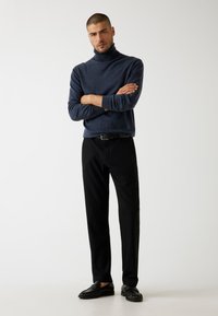 Dunkelblauer Rollkragenpullover, kombiniert mit schwarzen Hosen und schwarzen Slippers. Minimalistisches Design, glatte Textur und taillierte Silhouette.
