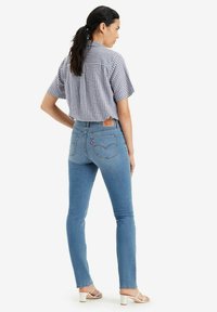 Jeans skinny in denim azzurro chiaro con vita alta e tasche posteriori; abbinati a una camicia a maniche corte a quadri e sandali bianchi con tacco.