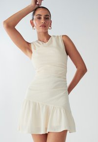 Helevalge kreemjas kleit, millel on vormis ülakehaosa, kärjemelised varrukad, keeratud kaelus ja laienenud volangiline alumineäär. Valmistatud tekstuurse kangaga, millel on peened detailid.