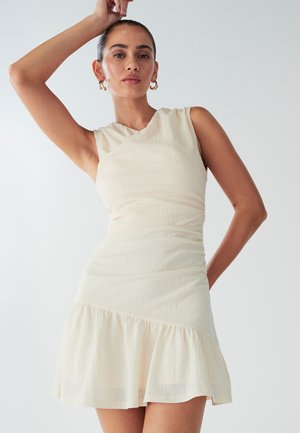 Abito senza maniche color crema con un corsetto aderente e un orlo a volant svasato. Tessuto testurizzato con leggere pieghe in vita.