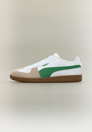 Lavprofils hvid Puma sneaker med grøn stribe, beige ruskind tåhætte og brun gummisål på neutral baggrund.