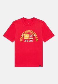 Red cotton t-shirt with short sleeves, featuring a graphic of two stylized sandwich characters and the text "PEANUT BUTTER AND ADI" in yellow.