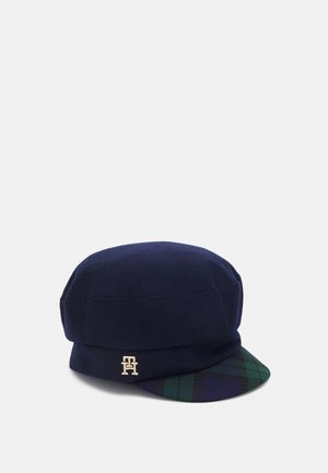 Casquette en laine bleu marine avec une visière à carreaux verts et bleu marine et un petit logo doré "TH" sur le côté.