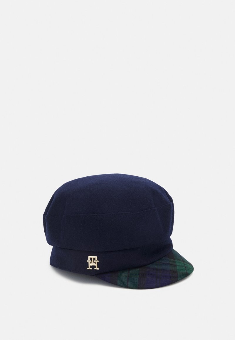Casquette en laine bleu marine avec une visière à carreaux verts et bleu marine et un petit logo doré "TH" sur le côté.