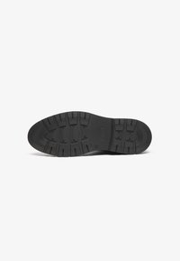 Suela de zapato de goma negra con patrón de textura, que presenta surcos profundos y bordes redondeados para tracción y estabilidad.