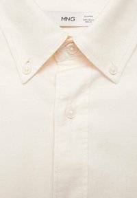 Crème-kleurig katoenen shirt met een klassieke kraag, voorzien van zes knoopsluitingen en een gestructureerde stof. Etiket leest "MNG Classic."