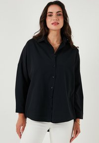 Camicia nera a maniche lunghe con colletto, dalla vestibilità rilassata, realizzata in tessuto morbido, abbinata a jeans bianchi.