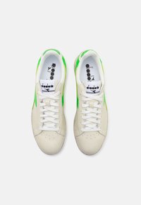 Sneakers in pelle bianca con accenti verdi, con punta arrotondata, lacci piatti e perforazioni sulla parte anteriore. Logo visibile sulla linguetta.