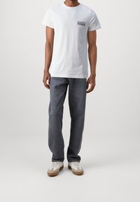 Bílý krátký rukáv tričko s malou nášivkou na prsou, v kombinaci s volnými tmavě šedými denimovými džínami a béžovými teniskami.