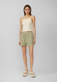 Lichtbeige cropped tanktop en groene textuurshorts met een elastische tailleband. Het model draagt beige platform sandalen. Eenvoudig ontwerp.