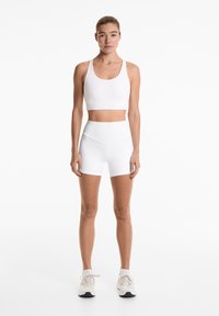 White sports bra with wide straps and a seamless design, paired with high-waisted white shorts. Suitable for active wear.