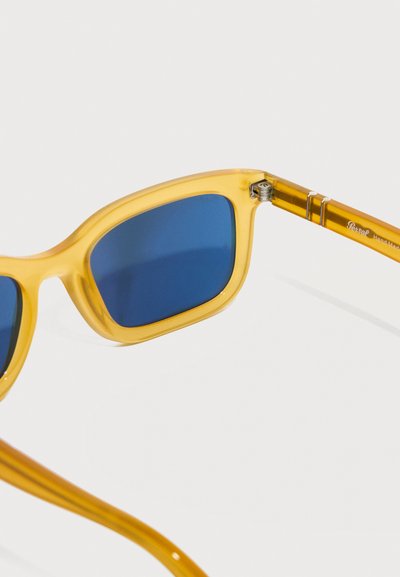 Κίτρινα ημιδιαφανή γυαλιά ηλίου με ορθογώνιους μπλε φακούς και ορατή ασημί λεπτομέρεια άρθρωσης στη βέργα.