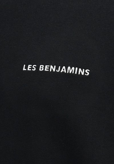 Μαύρο ύφασμα με λευκό κεντημένο κείμενο "LES BENJAMINS" στο κέντρο της επιφάνειας.