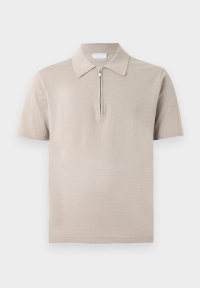 Polo beige à manches courtes avec col et demi-fermeture éclair sur le devant, présenté sur un fond uni gris clair.