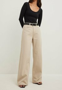 Top nero a maniche lunghe abbinato a pantaloni beige a gamba larga, dotati di una cintura. Materiale morbido, top aderente con scollatura a barca.