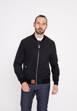 Sort bomberjakke med en frontlynlås, ribbede manchetter og en orange label; har sidelommer og et glat, let stof.