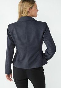 Dark pinstriped blazer with a tailored fit, notched lapels, and long sleeves, paired with fitted black pants. Smooth fabric texture.