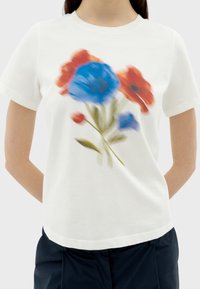 Witte t-shirt met korte mouwen, voorzien van een bloemenprint met blauwe en rode bloemen, groene stelen en een ontspannen pasvorm. Zacht katoen materiaal.