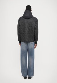 Schwarze gesteppte Jacke mit Kapuze, kombiniert mit lockeren blauen Jeans. Die Jacke hat eine strukturierte Oberfläche und gerippte Bündchen.