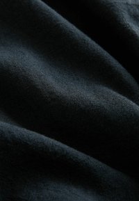 Sötét szövet, puha, texturált felülettel, ami finom fényt és lágy esést mutat. Az anyag vastagnak és tartósnak tűnik.