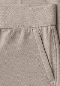 Jasnobeżowa teksturowana tkanina z pasem w talii i boczną kieszenią, ozdobiona subtelnymi marszczeniami i detalami szwów.