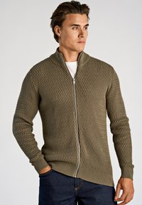 Oliijfgroene gebreide trui met ritssluiting, met een ruitpatroon en geribbelde manchetten. Heeft een hoge kraag en een rechte snit aan de zoom.