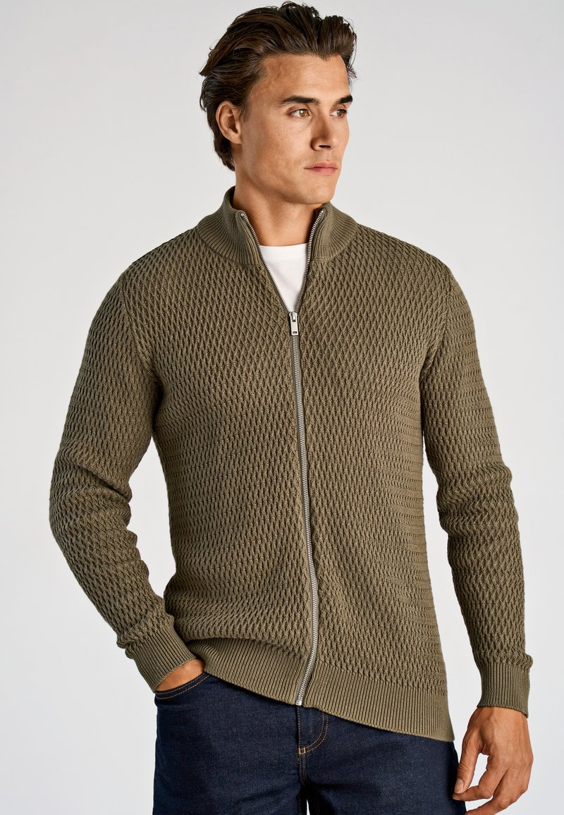 Oliijfgroene gebreide trui met ritssluiting, met een ruitpatroon en geribbelde manchetten. Heeft een hoge kraag en een rechte snit aan de zoom.