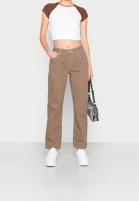 Bruna vida byxor i kraftigt tyg, matchade med en vit och brun kortärmad t-shirt. Kompletteras med vita sneakers och en mönstrad handväska.