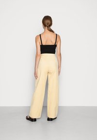 Zwarte geribde tanktop gecombineerd met lichtgele wijde corduroy broek. De broek heeft een hoge taille en twee achterzakken. Zwarte platform sandalen.