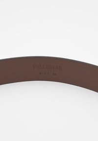 Barna bőrbelt, melyen dombornyomott "PULL&BEAR" márkázás és "SIZE 85" címke található. Simább textúra, ívelt forma és minimális design.